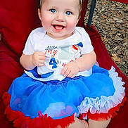 Kathleen joined the competition — help win amazing prizes! baby, child, smiling, blue_eyes, headband, dress, sitting, red_chair, outdoor, happy, cute, person, toddler, colorful_clothing, feet, face, celebration, holiday, fun, portrait