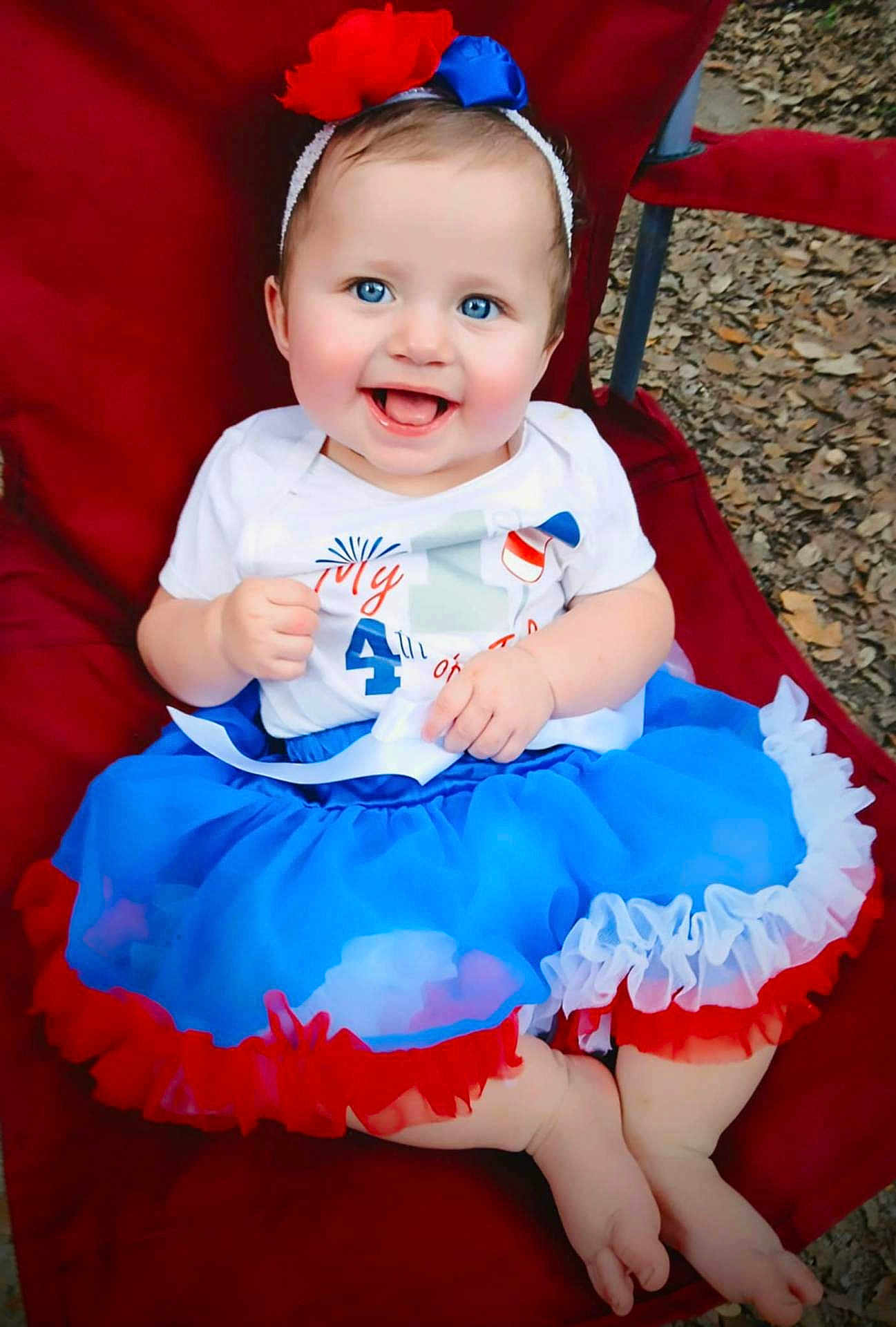 Kathleen joined the competition — help win amazing prizes! baby, child, smiling, blue_eyes, headband, dress, sitting, red_chair, outdoor, happy, cute, person, toddler, colorful_clothing, feet, face, celebration, holiday, fun, portrait