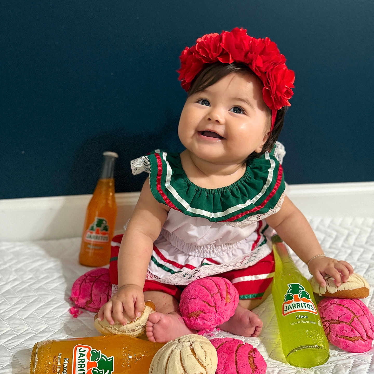 Ximena Liliana is registered to the contest to win money with this photo: baby, bread, celebration, child, colorful, conchas, cute, dress, feet, flower_crown, food, happy, headband, indoor, jarritos, sitting, smiling, snack, soda_bottle, white_bedspread