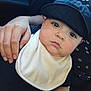 Anthony joined the competition — help win amazing prizes! baby, child, infant, hat, bib, hand, bracelet, person, face, skin, clothing, dark_background, patterned_clothing, closeup, expression, casual, indoor, holding, portrait, cute