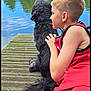 Oreo participe au concours pour gagner de l'argent avec cette photo : boy, dog, lake, dock, water, trees, sky, outdoor, grass, nature, pet, child, summer, relaxing, red_clothing, black_dog, calm, reflection, daytime, scenic
