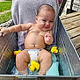 baby, water, rubber_duck, tub, diaper, smile, towel, outdoor, grass, wooden_deck, metal_container, child, playful, cute, relaxing, summer, bare_chest, infant, water_play, cheeky