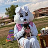 person_in_costume, easter_bunny, dog, small_dog, pink_outfit, outdoor, grass, spring, easter_eggs, decorations, chair, sky, clouds, tree, house, table, festive, holiday, celebration, leash