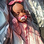 baby, pacifier, headband, pink_clothing, bedspread, sunlight, infant, sleepwear, blanket, indoor, resting, cute, child, face, hands, soft_light, pattern, cozy, portrait, sleeping