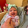 baby, infant, smiling, headband, hand_holding, couch, person, child, indoor, holiday_decor, santa_figure, happy, face, clothing, adult_hand, cute, portrait, cozy, home, family