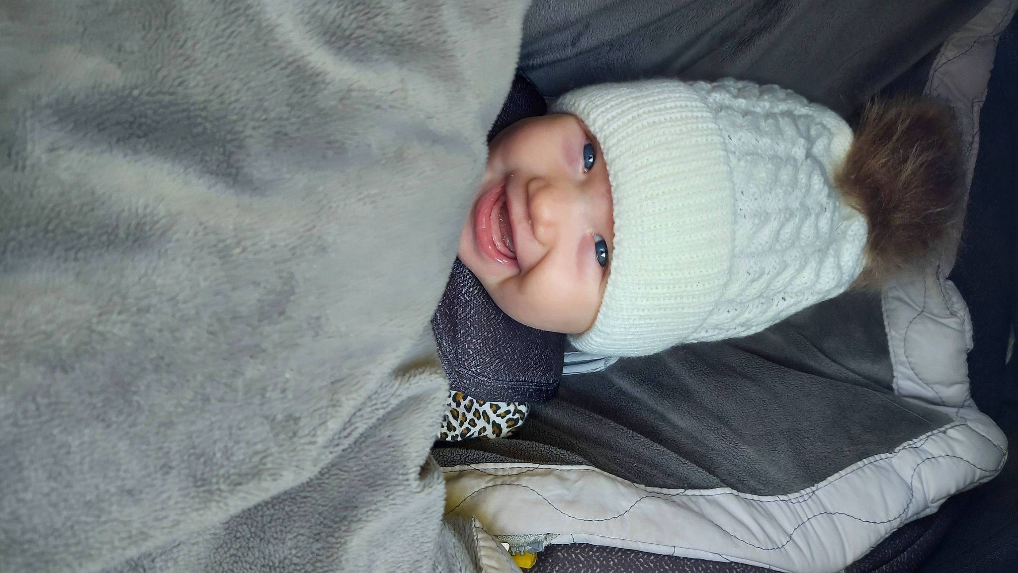 Mackenna joined the competition — help win amazing prizes! baby, baby_toddler_clothing, cheek, child, comfort, fur, grey, headwear, human_body, knit_cap, linens, person, sitting, sleeve, smile, textile, toddler, tree, winter, wool