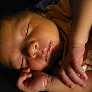 River is registered to the contest to win money with this photo: baby, sleeping, face, hand, infant, closeup, peaceful, skin, newborn, portrait, cute, resting, soft_light, yellow_clothing, dark_background, tiny_fingers, calm, indoors, child, relaxation
