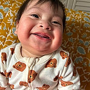 Liam is registered to the contest to win money with this photo: baby, child, smiling, face, onesie, bear_pattern, clothing, cheeks, happy, indoor, portrait, young_child, cute, infant, person, closeup, head, expression, sitting, background