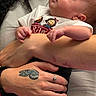 Lorenzo is registered to the contest to win money with this photo: baby, newborn, infant, arms, hand, tattoo, ring, clothing, person, sleeping, cute, skin, holding, white_shirt, cartoon, name_text, closeup, love, peaceful, portrait