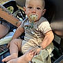 baby, pacifier, hat, tattoo, arm, leather_seat, child, infant, outdoor, wood, deck, curious, calm, skin, short_sleeve, foot, hand, resting, seat_belt, person