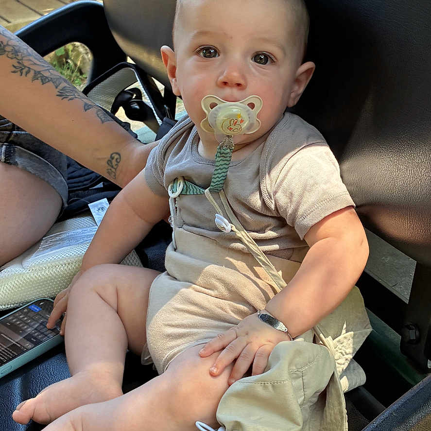 Ethan participe au concours pour gagner de l'argent avec cette photo : arm, baby, calm, child, curious, deck, foot, hand, hat, infant, leather_seat, outdoor, pacifier, person, resting, seat_belt, short_sleeve, skin, tattoo, wood