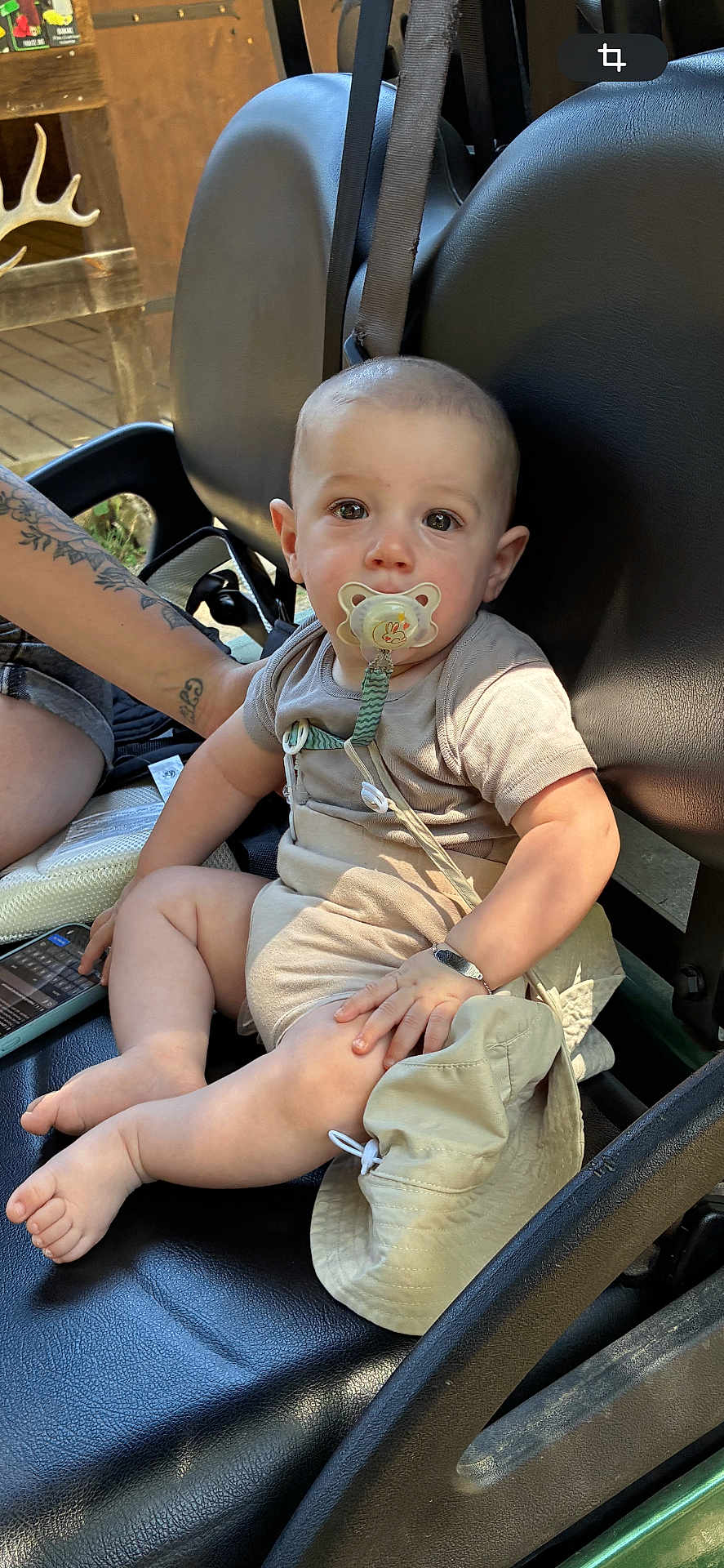 Ethan participe au concours pour gagner de l'argent avec cette photo : baby, pacifier, hat, tattoo, arm, leather_seat, child, infant, outdoor, wood, deck, curious, calm, skin, short_sleeve, foot, hand, resting, seat_belt, person
