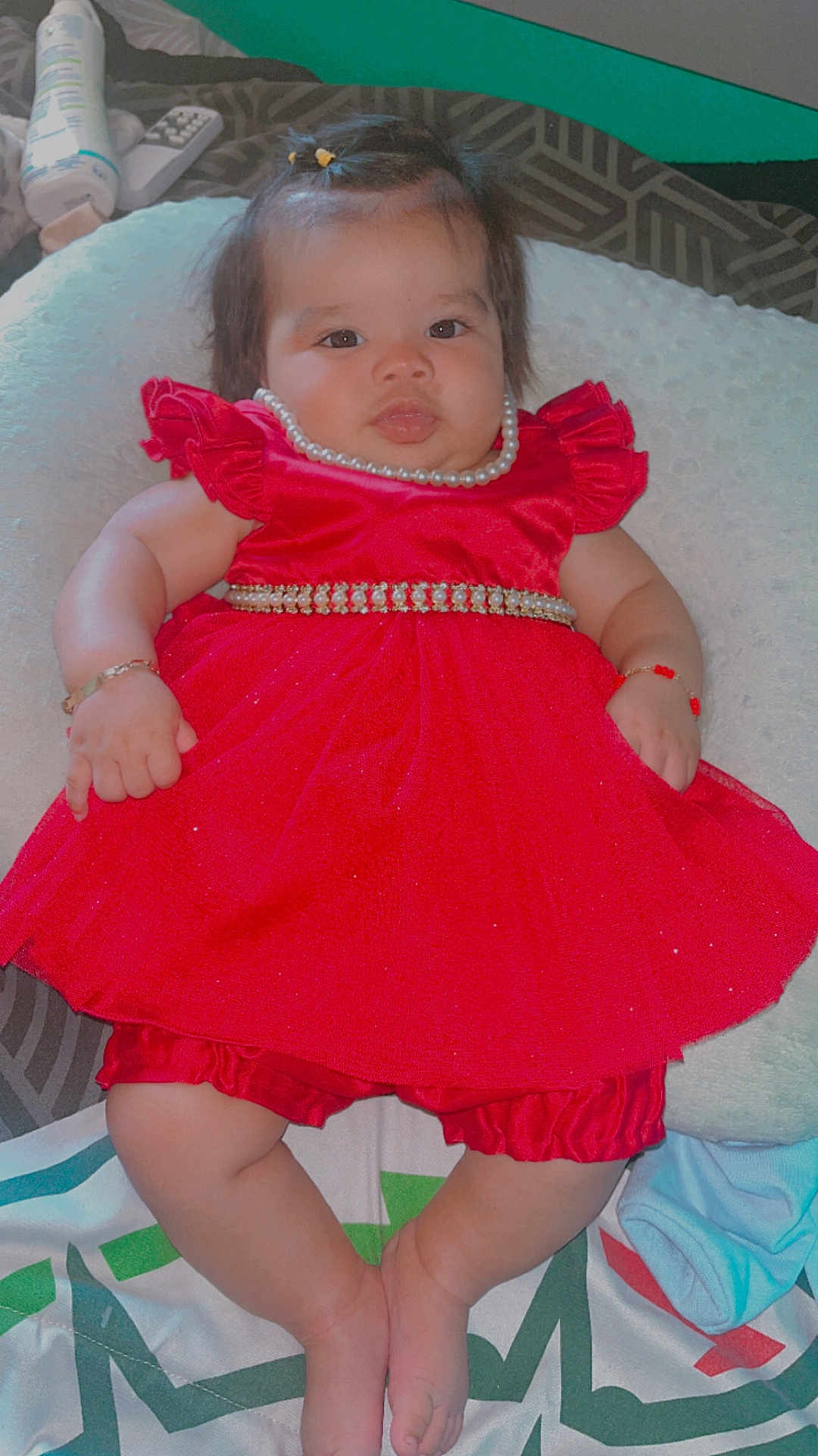 Georgina joined the competition — help win amazing prizes! baby, infant, red_dress, pearl_necklace, bracelet, cushion, blanket, indoor, cute, chubby_cheeks, baby_clothing, relaxed, portrait, person, soft_texture, lying_down, footwear_off, bed, accessories, adorable