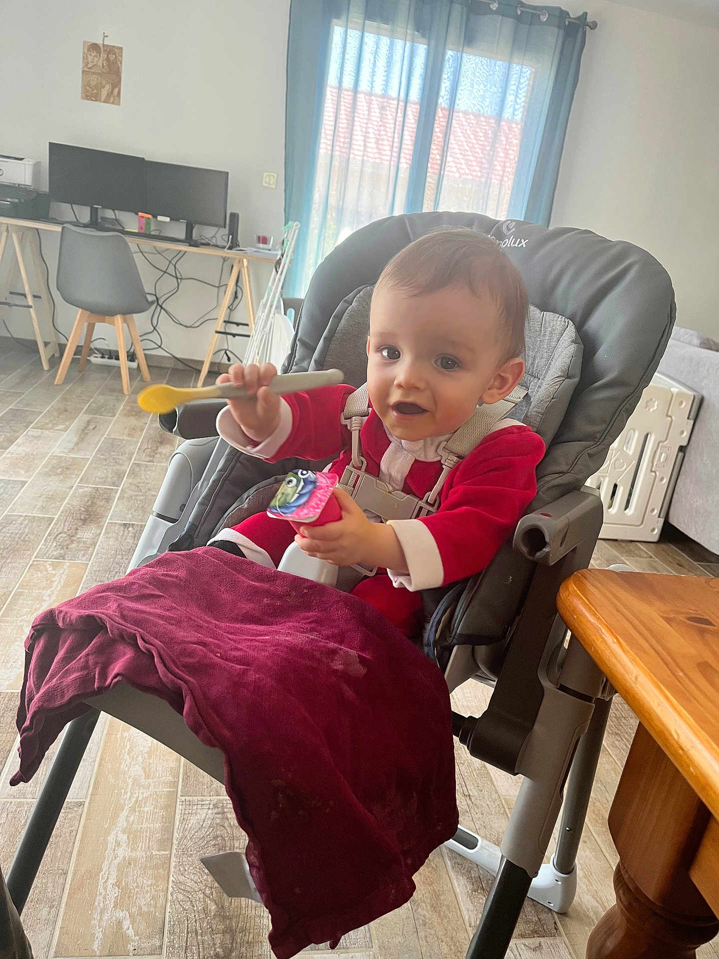 Celestin participe au concours pour gagner de l'argent avec cette photo : baby, high_chair, spoon, red_clothing, indoor, floor, table, curtains, window, computer, chair, desk, child, person, happy, feeding, snack, home, furniture, toddler