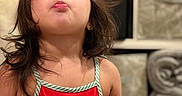 Maddie joined the competition — help win amazing prizes! child, girl, toddler, portrait, indoors, red_dress, watermelon_pattern, water_bottle, kissy_face, long_hair, brown_hair, standing, shelves, stuffed_animal, couch, home, smiling, playful, close_up, photography