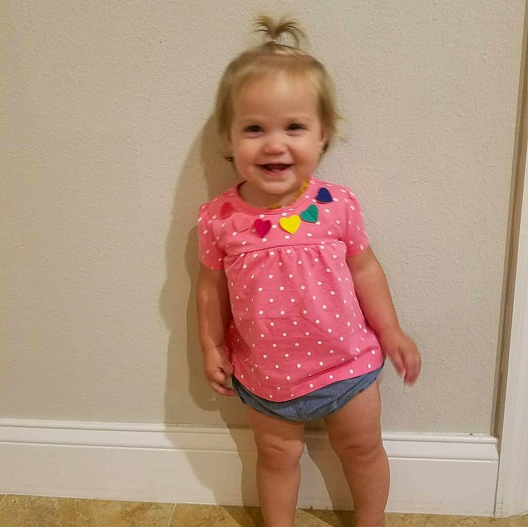 Max is registered to the contest to win money with this photo: abdomen, child, clothing, day, design, girl, human_hair_color, joy, neck, outerwear, pattern, person, pink, shorts, shoulder, sleeve, standing, t_shirt, textile, toddler