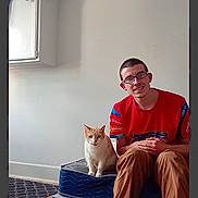 Scotty joined the competition — help win amazing prizes! blue_mattress, cabinet, carpet, casual_clothing, cat, glasses, home, indoor, man, mattress, orange_cat, pet, red_shirt, relaxed, short_hair, sitting, smiling, towel, white_cat, wooden_floor