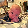 baby, infant, child, portrait, face, blue_eyes, looking_at_camera, resting, hands, blanket, checkered_blanket, bed, home, indoor, kitchen, baby_gear, warm_lighting, cozy, sitting, close_up