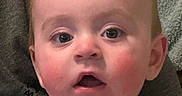 Caden is registered to the contest to win money with this photo: baby, infant, child, portrait, close_up, face, eyes, wide_eyed, expression, sitting, onesie, clothing, gray_background, indoor, couch, cozy, head, cheeks, photography, person