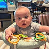Caden joined the competition — help win amazing prizes! baby, child, infant, wide_eyes, surprised, sitting, play_seat, toy, teether, colorful_toys, gray_shirt, portrait, indoor, home, kitchen, living_room, high_chair, playtime, face, candid