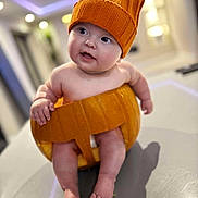 Arabella is registered to the contest to win money with this photo: baby, pumpkin, hat, infant, cute, indoor, table, chubby_cheeks, knitted, orange, holiday, fall, child, legs, toes, smiling, costume, portrait, sitting, curious