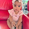 baby, child, pink_bow, headband, pink_clothing, red_chair, leather_chair, indoors, cute, sitting, shoe, curious, infant, portrait, toddler, furniture, home, person, smile, hands