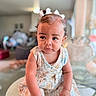 baby, blurred_background, child, curious, decor, expression, face, floral_dress, girl, glass_table, hair_bows, hands, home, indoor, person, portrait, seated, skin, soft_lighting, toddler