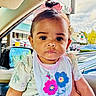 baby, bib, car_interior, car_window, child, clothing, curly_hair, cute, daylight, earrings, flower_pattern, girl, hand, little_princess, parking_lot, person, pink_bow, portrait, serious_expression, toddler