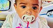 Dioř Aahmoř is registered to the contest to win money with this photo: baby, pacifier, bib, pink_bow, curly_hair, child, indoor, car_interior, hand, flowers, clothing, cute, portrait, person, young_child, window, seat, colorful, expression, closeup