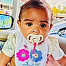 baby, bib, car_interior, child, closeup, clothing, colorful, curly_hair, cute, expression, flowers, hand, indoor, pacifier, person, pink_bow, portrait, seat, window, young_child