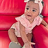 Dioř Aahmoř is registered to the contest to win money with this photo: baby, child, pink_outfit, headband, bow, red_couch, leather, smiling, happy, indoor, cute, infant, sitting, footwear, shoe, hand, portrait, person, curious, bright_eyes