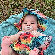 Emory is registered to the contest to win money with this photo: baby, infant, pacifier, colorful_clothing, hat, towel, grass, outdoor, feet, playful, cute, child, summer, toddler, nature, lying_down, skin, face, expressionless, barefoot