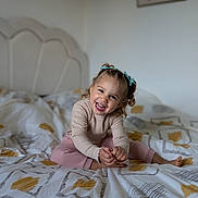 Joy participe au concours pour gagner de l'argent avec cette photo : child, toddler, smiling, happy, bed, bedding, blanket, indoor, person, cute, hair_bows, long_sleeve_shirt, pink_pants, feet, hands, head, face, home, cozy, playful