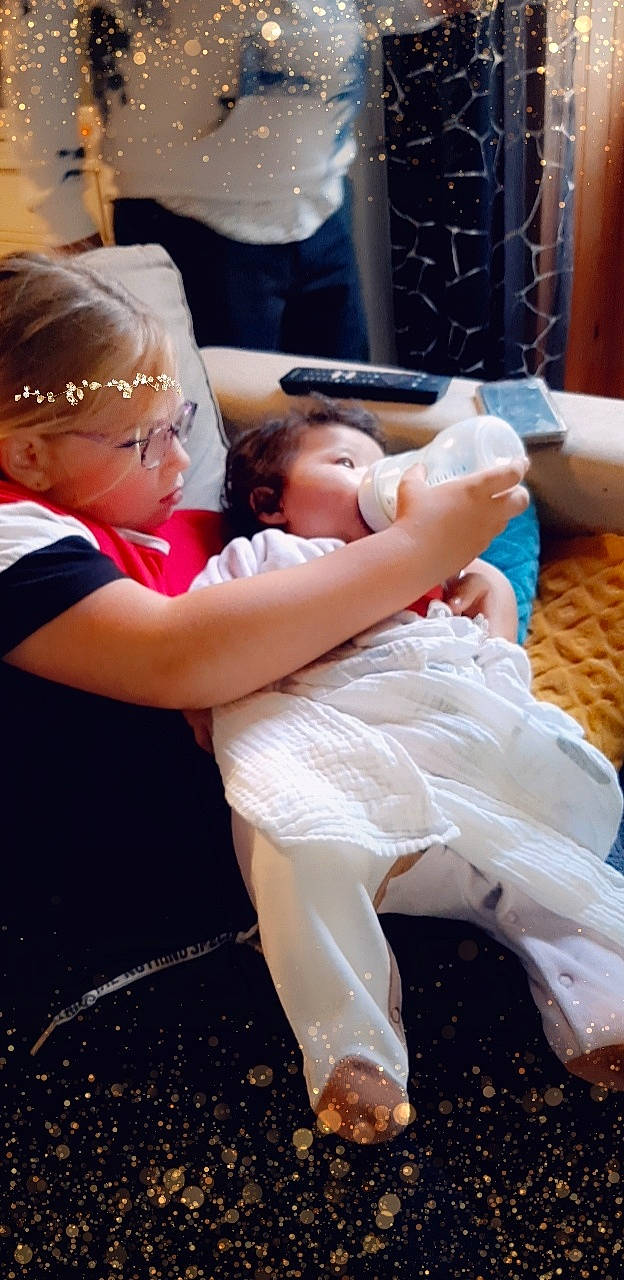 Tahina participe au concours pour gagner de l'argent avec cette photo : baby, bridal_clothing, cap, child, comfort, couch, dress, event, flash_photography, formal_wear, fun, gesture, happy, human_leg, interaction, person, sitting, thigh, toddler, tradition