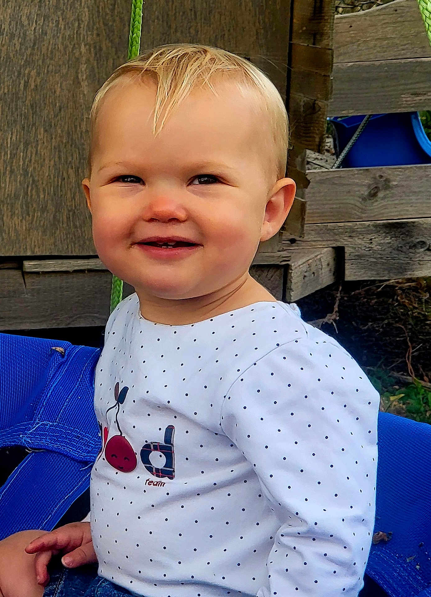 Armelle a rejoint le concours — aidez-le/la à gagner de superbes lots ! toddler, child, smiling, outdoor, swing, blue, white_shirt, polka_dot, cherry_design, wooden_background, happy, face, cute, playground, casual_clothing, person, nature, daylight, portrait, sitting
