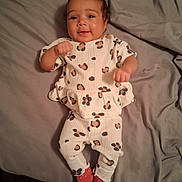 Heavenly is registered to the contest to win money with this photo: baby, child, infant, portrait, smiling, lying_down, bed, bedding, indoors, clothing, outfit, patterned_clothing, red_socks, hands, fists, face, head, cozy, happy, photograph