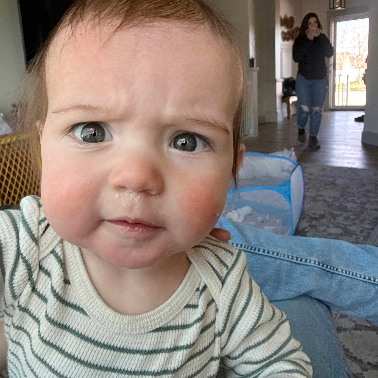 Daniel is registered to the contest to win money with this photo: baby, child, face, person, indoor, living_room, curious, expression, striped_shirt, drool, blurred_background, woman, walking, home, playpen, carpet, jeans, casual_clothing, furniture, light