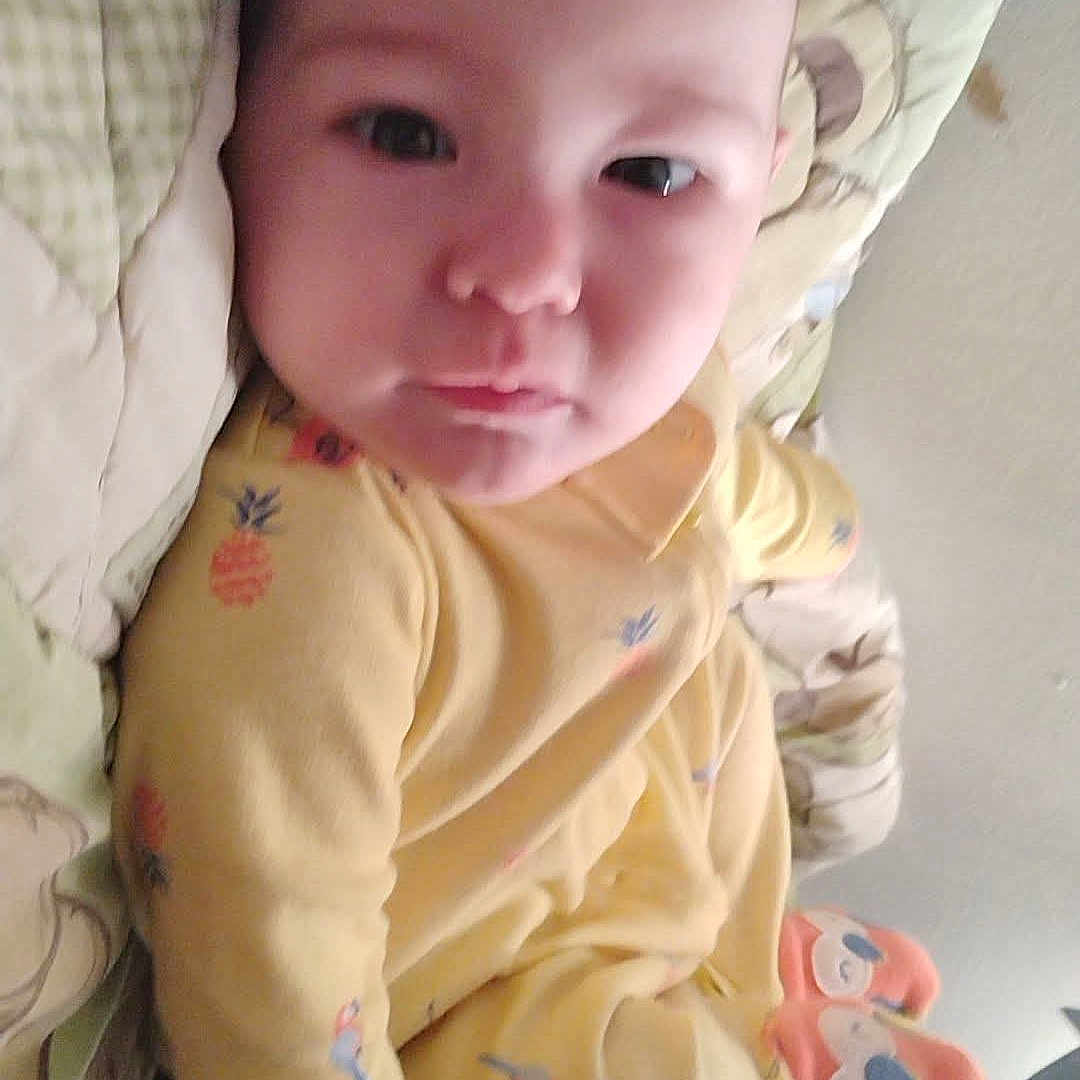 Ma'Kia Slapnicka is registered to the contest to win money with this photo: baby, blanket, child, cushion, cute, expression, eyes, face, footwear, head, indoor, infant, lying_down, patterned_clothing, person, plush_toy, skin, sleepwear, soft_fabric, yellow_onesie