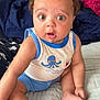 baby, child, curly_hair, blue_shorts, tank_top, octopus_print, bed, blanket, cushion, indoors, cute, wide_eyes, surprised_expression, skin, foot, hand, person, sitting, infant, soft_fabric