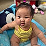 baby, child, sitting, yellow_clothing, blue_cushion, indoors, face, hair_tie, toy, blurred_background, cute, chubby_cheeks, person, infant, smiling, plush, soft, comfortable, home, curious
