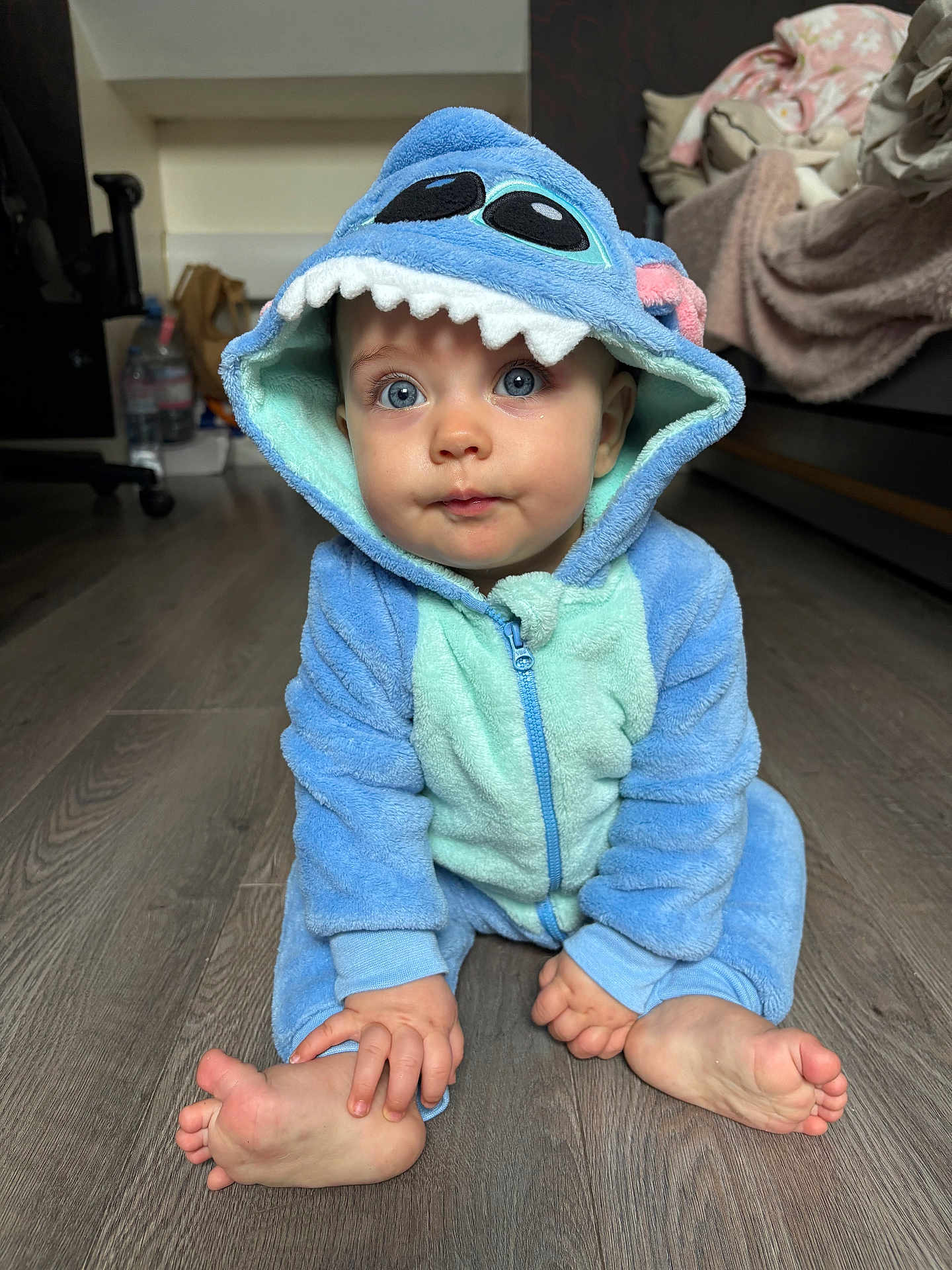 Isadora a rejoint le concours — aidez-le/la à gagner de superbes lots ! baby, child, blue_onesie, dinosaur_costume, hood, floor, wooden_floor, sitting, barefoot, hand, foot, indoor, curious, cute, face, expression, person, cozy, home, clothing