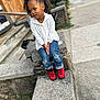 Asiyah Sareal is registered to the contest to win money with this photo: child, curly_hair, white_hoodie, blue_jeans, red_shoes, concrete, outdoor, sidewalk, stairs, pom_pom_hair_accessories, casual_clothing, urban, residential_area, young_girl, sitting, curious_expression, daylight, portrait, street, fashion