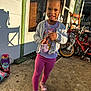 child, girl, braids, purple_bow, pink_leggings, sneakers, bugs_bunny, cardigan, roller_skates, bicycle, porch, sunlight, concrete, door, window, shadow, outdoor, play, happy, casual_clothing