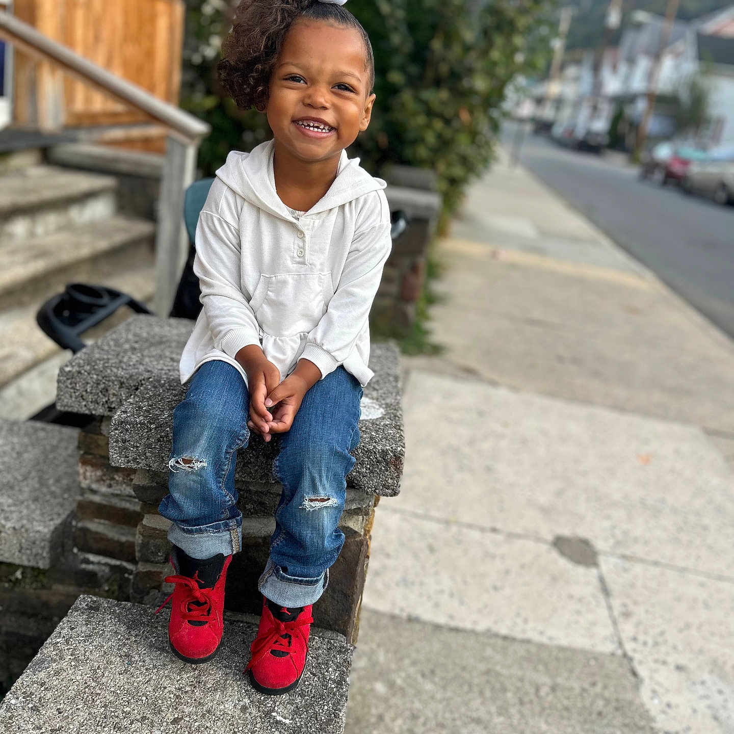 Asiyah Sareal is registered to the contest to win money with this photo: casual_clothing, child, concrete, curly_hair, daylight, greenery, happy, hoodie, jeans, outdoor, playful, portrait, red_shoes, sidewalk, sitting, smile, steps, stone, street, urban