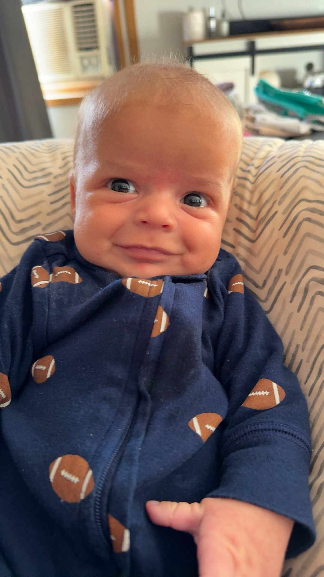 Dawson joined the competition — help win amazing prizes! baby, infant, smile, face, hand, clothing, football_pattern, cushion, striped, indoor, air_conditioner, background, person, portrait, cute, child, young, cozy, relaxing, home