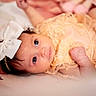 baby, infant, bow, headband, lace, peach, clothing, face, eyes, portrait, cute, newborn, soft_focus, lying_down, baby_girl, skin, expression, closeup, adorable, background