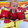 toddler, child, inflatable_pool, floaties, spiderman, water_toy, outdoor, summer, playtime, swimwear, red, yellow, blue, skin, face, hair, foot, grass, tree, building