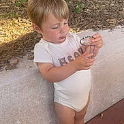Gohan a rejoint le concours — aidez-le/la à gagner de superbes lots ! toddler, child, outdoor, onesie, bracelet, beads, footwear, blue_shoes, standing, curious, nature, plants, mulch, stone_wall, sunlight, short_hair, casual_clothing, person, young_child, daylight