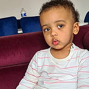 Matteo participe au concours pour gagner de l'argent avec cette photo : toddler, child, indoor, couch, maroon, striped_shirt, curly_hair, thoughtful, seated, furniture, water_bottle, blue_chair, casual_clothing, portrait, young_child, expression, face, person, home, relaxed