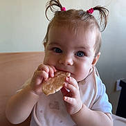 Eliana participe au concours pour gagner de l'argent avec cette photo : baby, bib, biscuits, blue_eyes, child, clothing, cute, eating, face, food, hand, happy, high_chair, indoor, infant, light, person, pigtails, skin, table